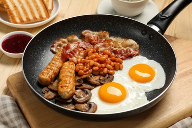 Frying pan with cooked traditional English breakfast on wooden table, closeup