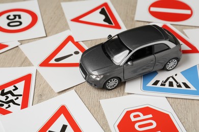 Photo of Cards with different road signs and toy car on wooden table. Driving school