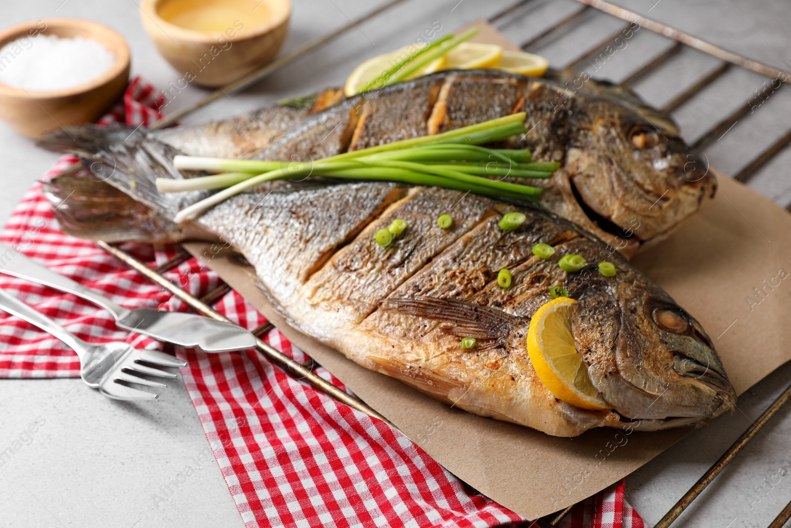 Photo of Seafood. Delicious baked fish served with green onion and lemon on light table, closeup