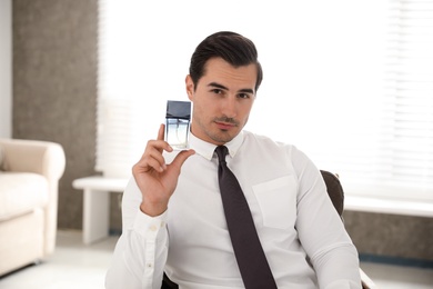 Handsome young man with bottle of perfume indoors