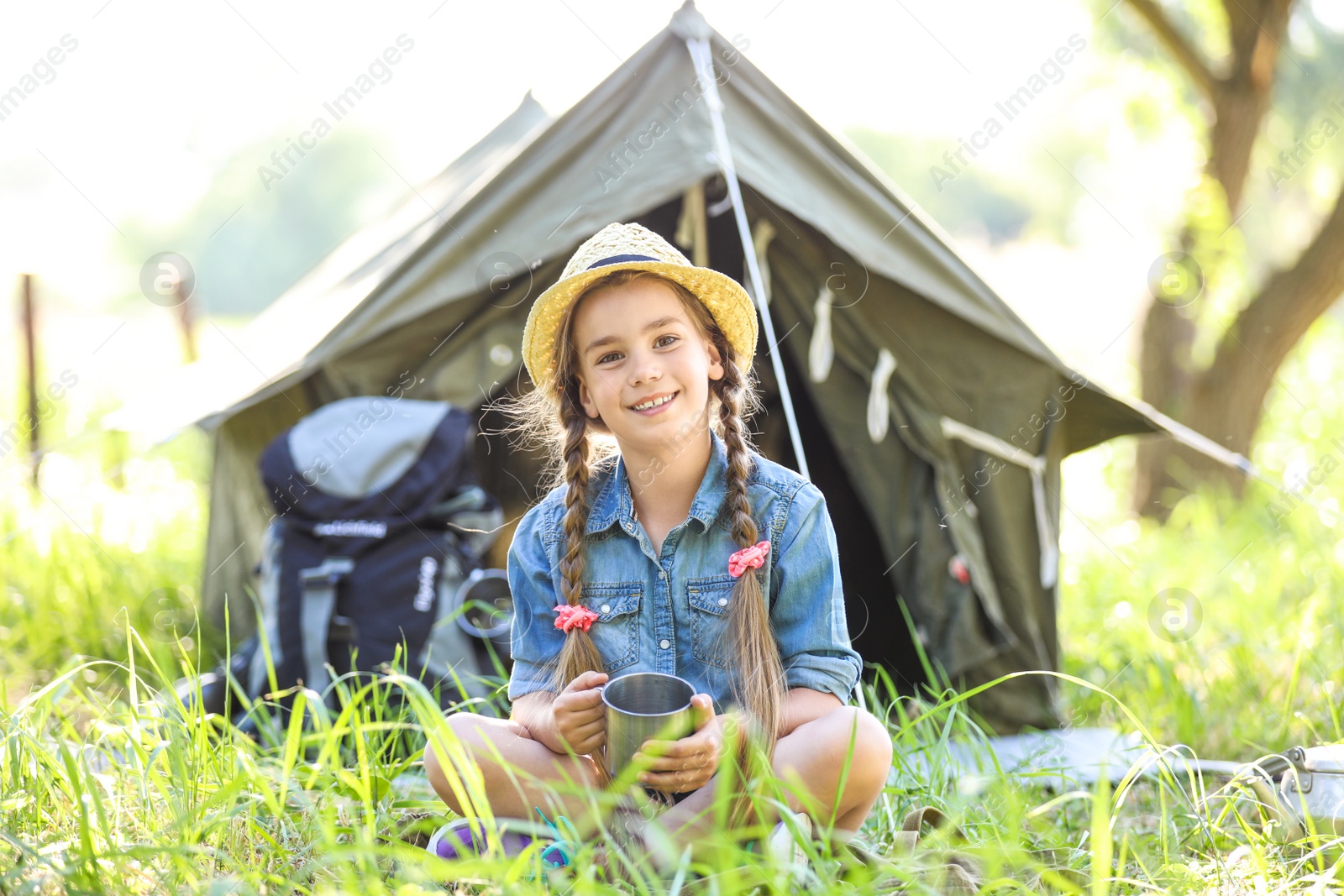 Photo of Little girl with mug near tent outdoors. Summer camp