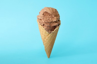 Delicious chocolate ice cream in waffle cone on light blue background