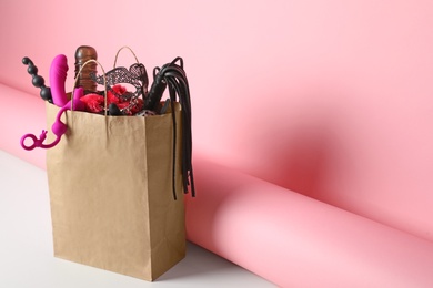 Photo of Paper shopping bag with different sex toys on pink background. Space for text