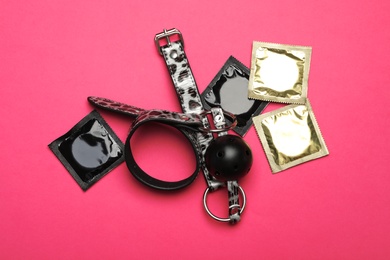 Ball gag and condoms on pink background, top view. Sex game