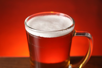 Photo of Mug with fresh beer on table against red background, closeup