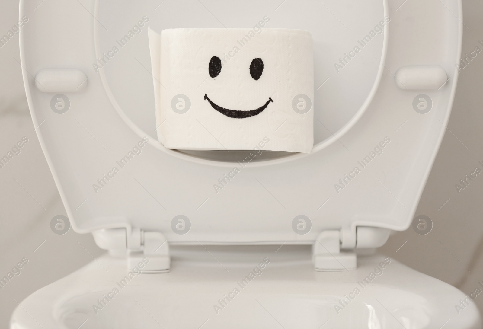 Photo of Roll of paper with funny face on toilet bowl in bathroom, closeup