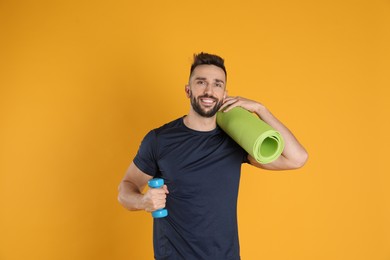 Photo of Handsome man with yoga mat and dumbbell on yellow background