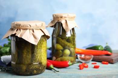 Photo of Jars with pickled cucumbers on wooden table against blue background, space for text