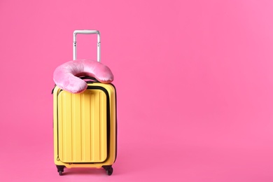 Photo of Yellow suitcase and travel pillow on pink background, space for text