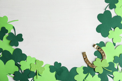 Photo of Flat lay composition with clover leaves and horseshoe on white wooden background, space for text. St. Patrick's day