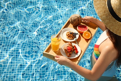 Young woman with delicious breakfast on tray in swimming pool, closeup. Space for text