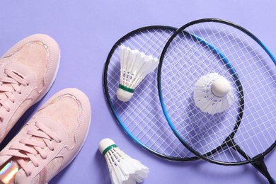 Feather badminton shuttlecocks, rackets and sneakers on violet background, flat lay