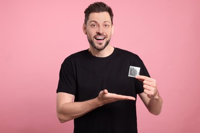 Photo of Excited man holding condom on pink background