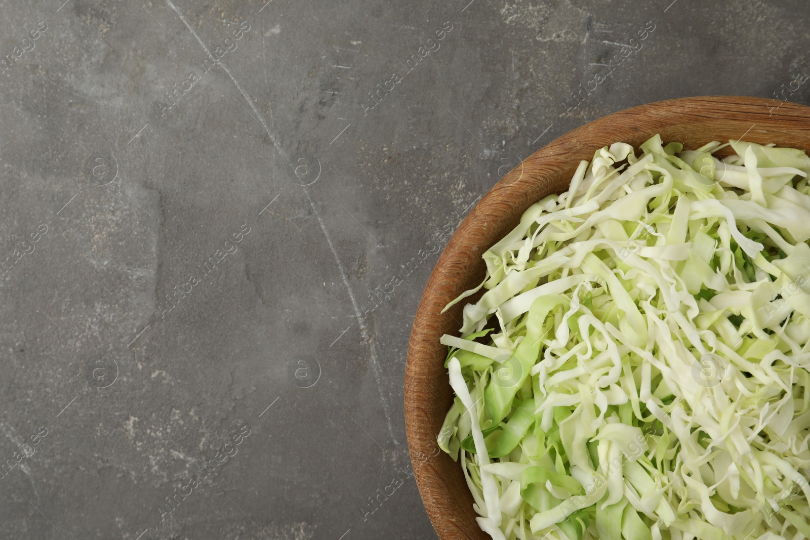 Photo of Chopped cabbage in bowl on grey table, top view. Space for text