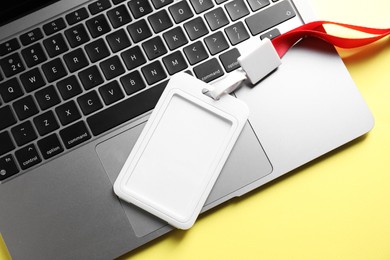 Photo of Blank badge and laptop on yellow background, top view