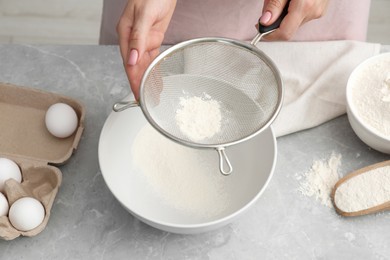 Making tasty baklava. Woman sifting flour into bowl at light grey marble table, above view