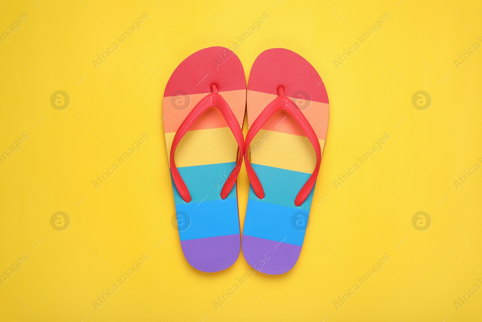 Photo of Rainbow flip flops on yellow background, flat lay. LGBT pride