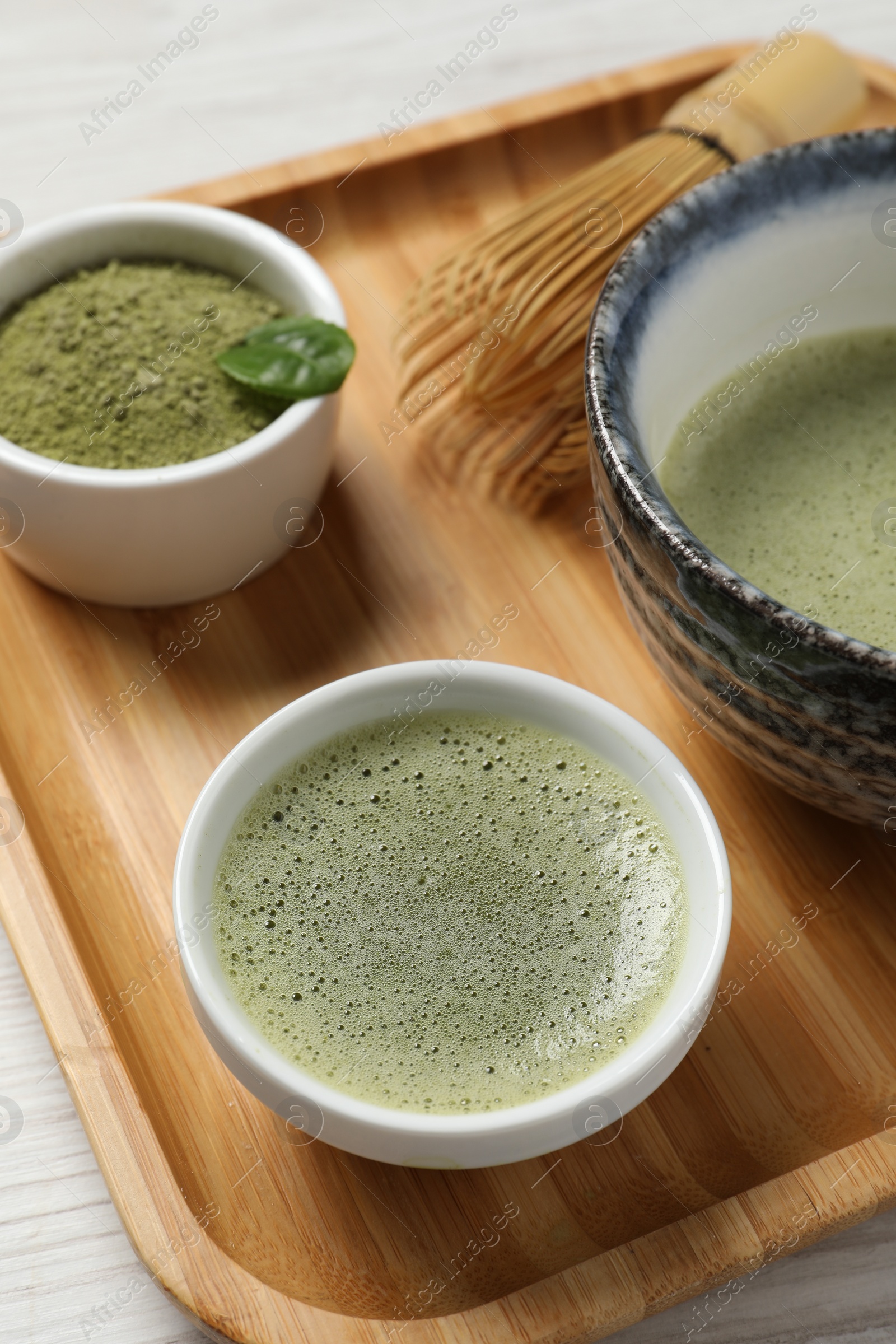 Photo of Fresh matcha tea, bamboo whisk and green powder on wooden tray, closeup