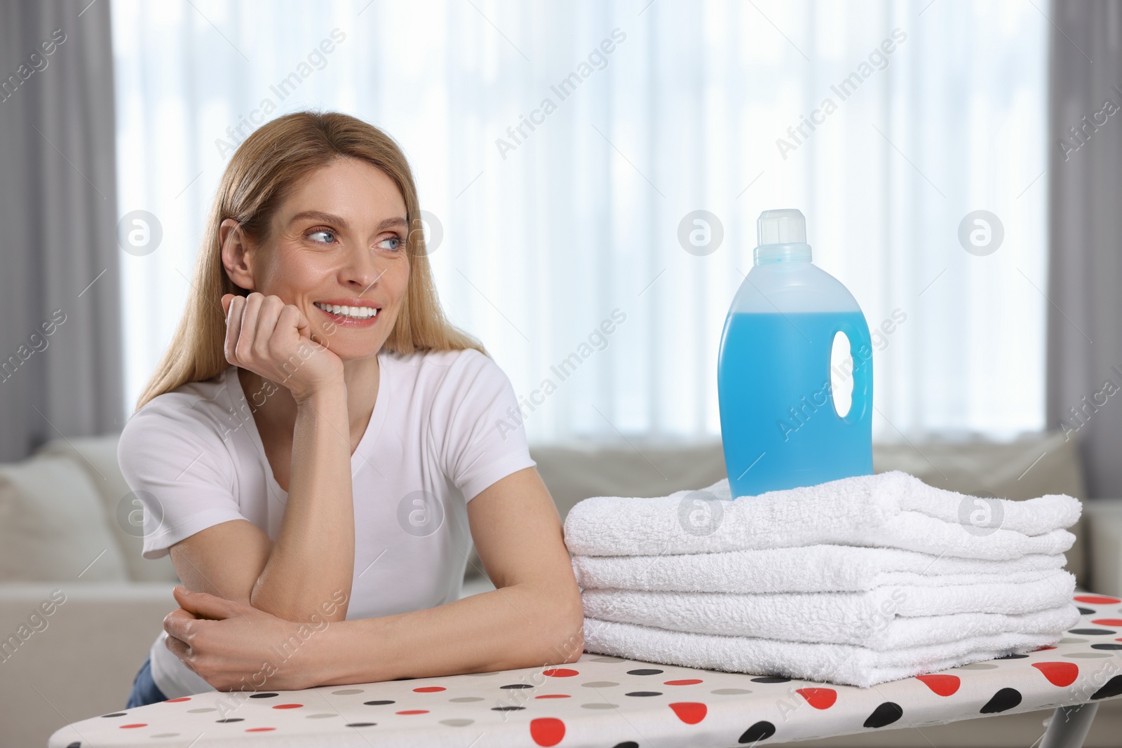 Photo of Woman with fabric softener and clean towels in room