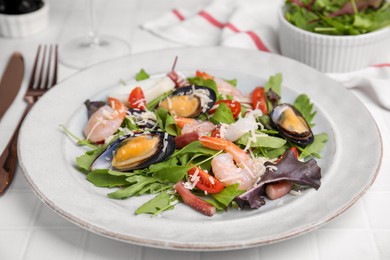 Plate of delicious salad with seafood on white tiled table, closeup
