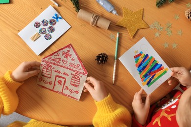 Little children with beautiful Christmas greeting cards at wooden table, top view