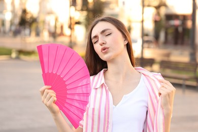 Woman with hand fan suffering from heat outdoors