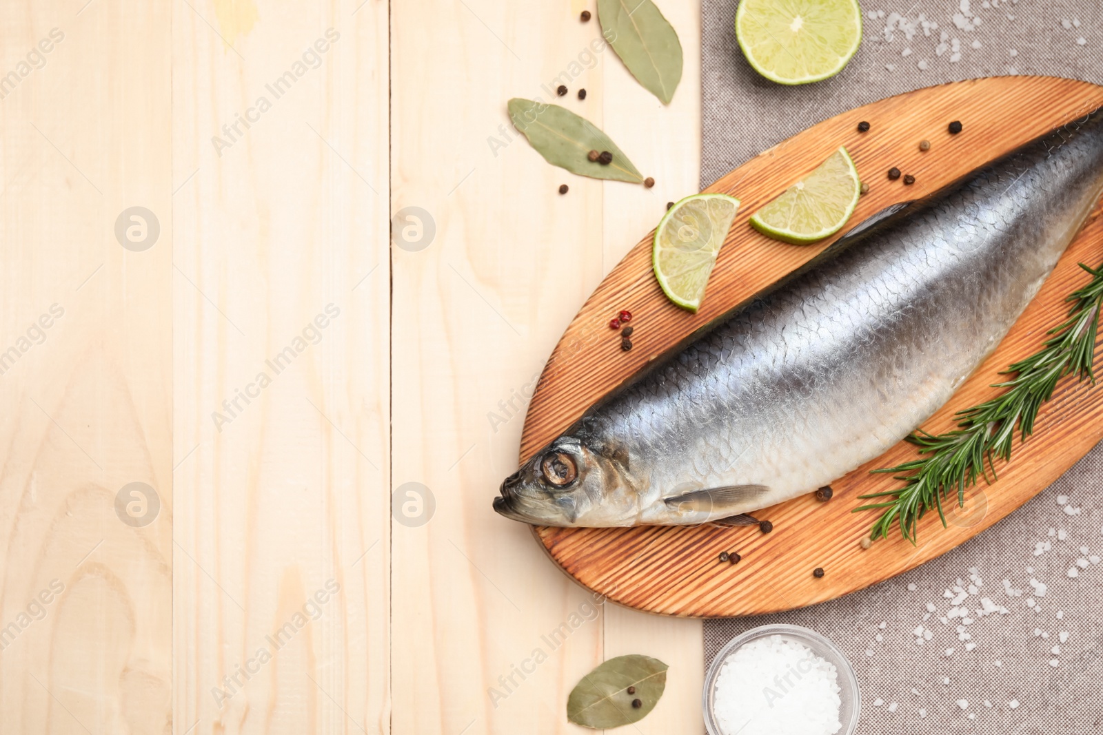 Photo of Delicious salted herring, bay leaves, lime, rosemary and salt on wooden table, flat lay. Space for text