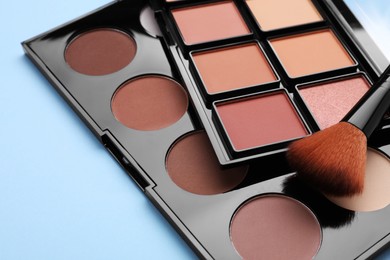 Photo of Contouring palettes and brush on light blue background, closeup. Professional cosmetic product