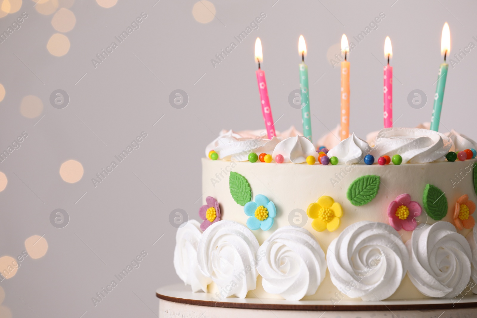 Photo of Delicious birthday cake with party decor on stand against blurred festive lights, closeup. Space for text