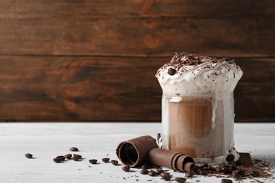 Photo of Glass cup of tasty coffee with whipped cream and chocolate on table. Space for text