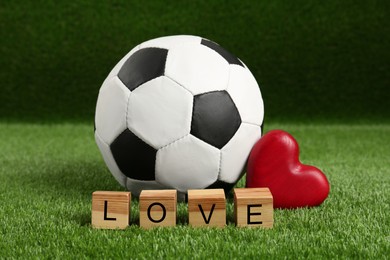 Soccer ball, heart and cubes with word Love on green grass