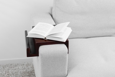 Open book on sofa with wooden armrest table indoors. Interior element