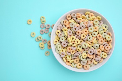 Photo of Tasty cereal rings in bowl on light blue table, top view. Space for text