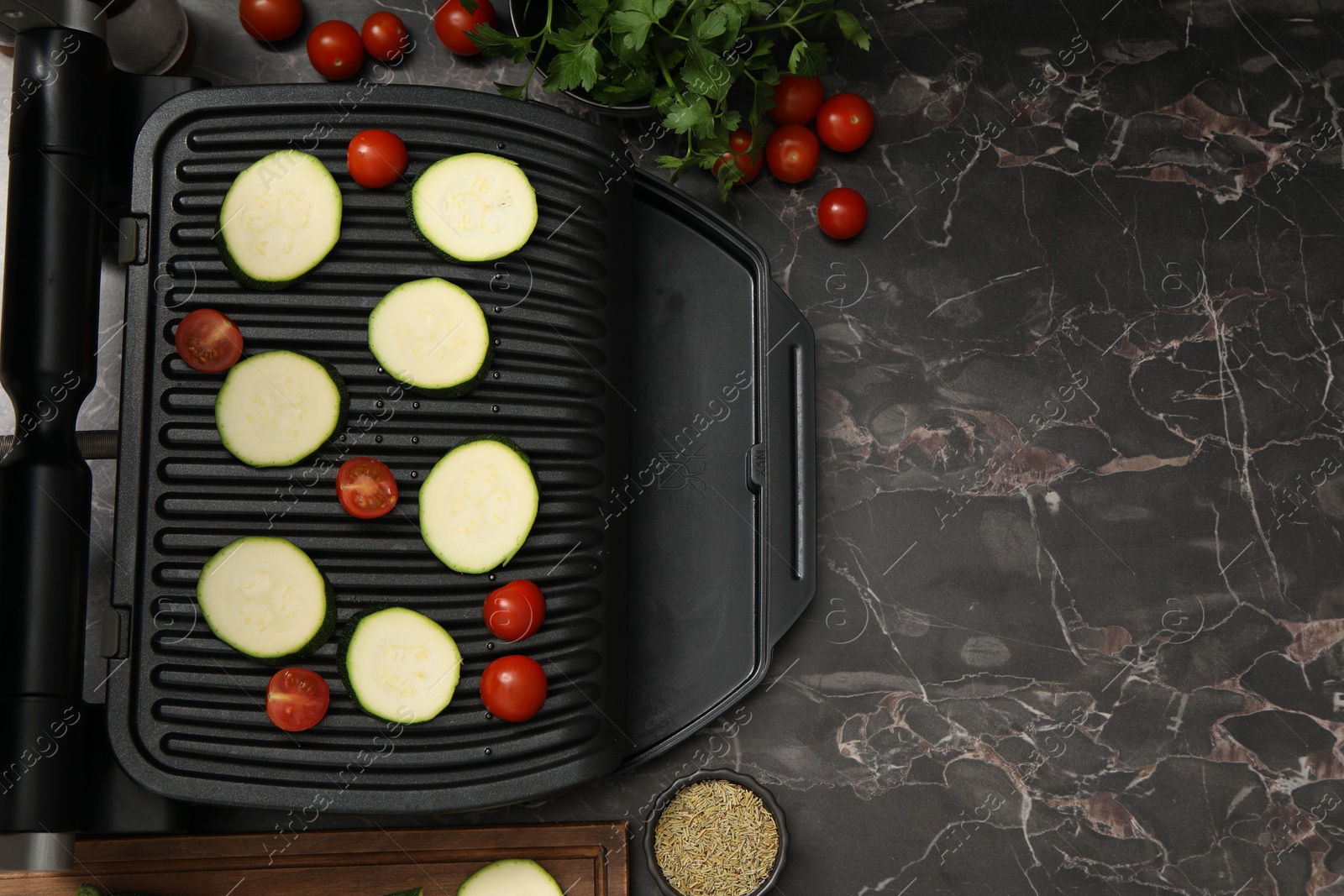 Photo of Electric grill with vegetables and spices on black marble table, flat lay. Space for text