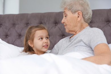 Photo of Cute girl and her grandmother reading book on bed at home