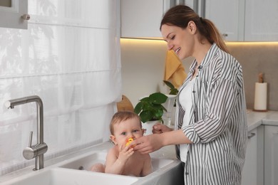 Mother washing her little baby in sink at home