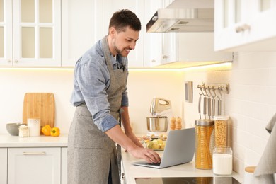 Photo of Man making dinner while watching online cooking course via laptop in kitchen