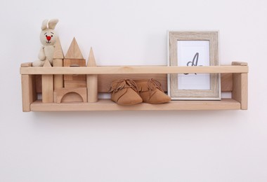 Wooden shelf with child's booties, toys and photo frame on white wall. Interior element