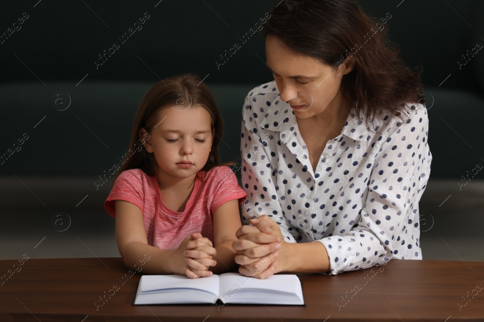 Photo of Mature woman with her little granddaughter praying together over Bible at home