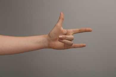 Photo of Woman showing gesture of horns on grey background, closeup