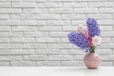 Photo of Beautiful hyacinths in pink vase on table against brick wall, space for text. Spring flowers