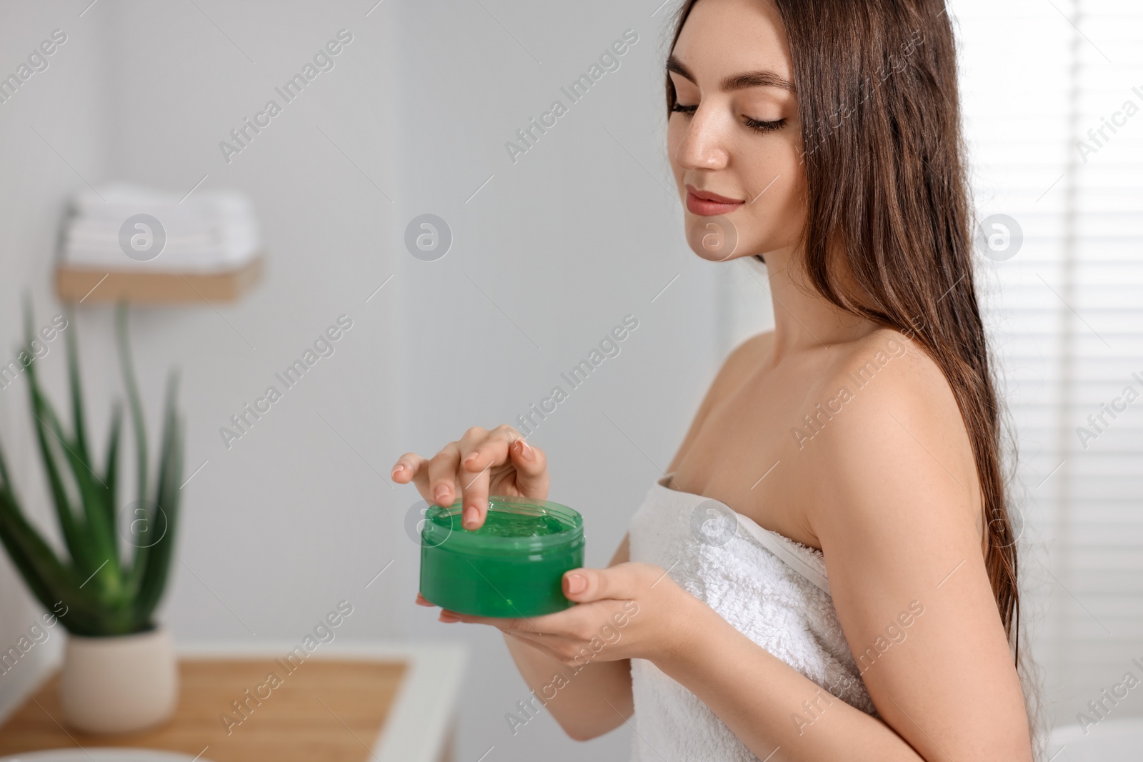 Photo of Young woman holding jar of aloe hair mask in bathroom. Space for text