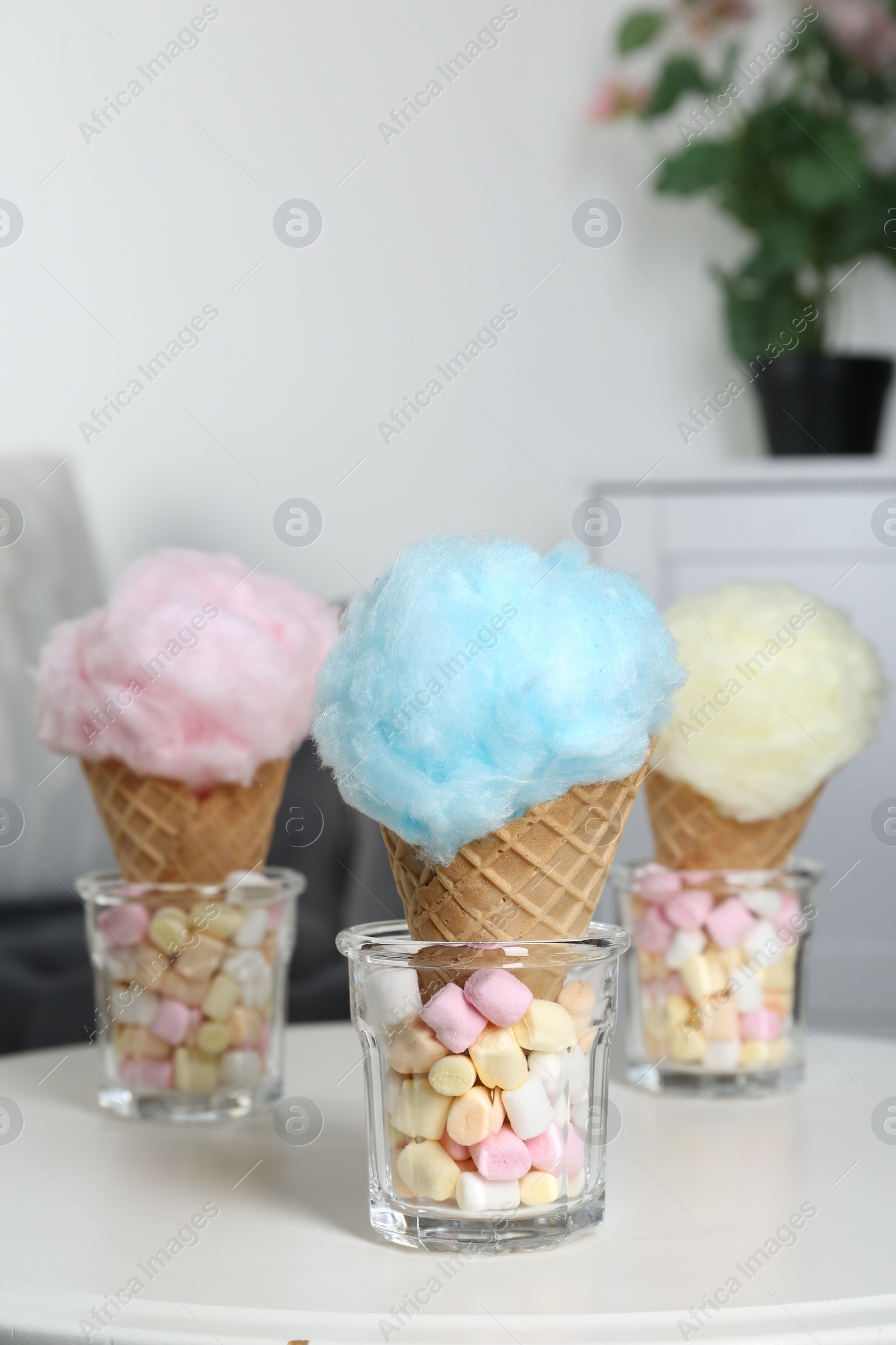 Photo of Sweet cotton candies in waffle cones and marshmallows on white table indoors, closeup