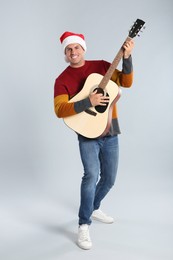 Photo of Man in Santa hat playing acoustic guitar on light grey background. Christmas music
