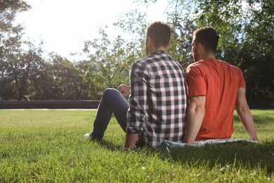 Photo of Gay couple sitting on green grass in park, back view