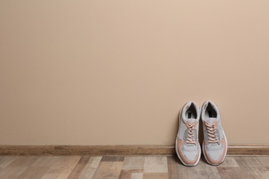 Photo of Pair of sport shoes on floor near color wall, space for text