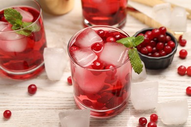 Photo of Tasty cranberry cocktail with ice cubes and mint in glasses on wooden table, closeup