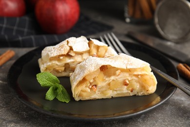 Photo of Delicious apple strudel with almonds, powdered sugar and mint on grey table