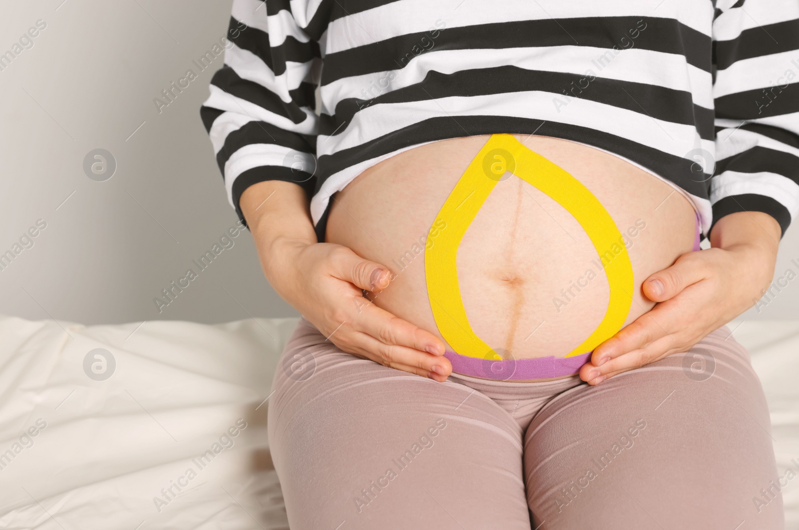 Photo of Pregnant woman with kinesio tapes on her belly indoors, closeup