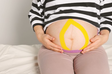 Photo of Pregnant woman with kinesio tapes on her belly indoors, closeup